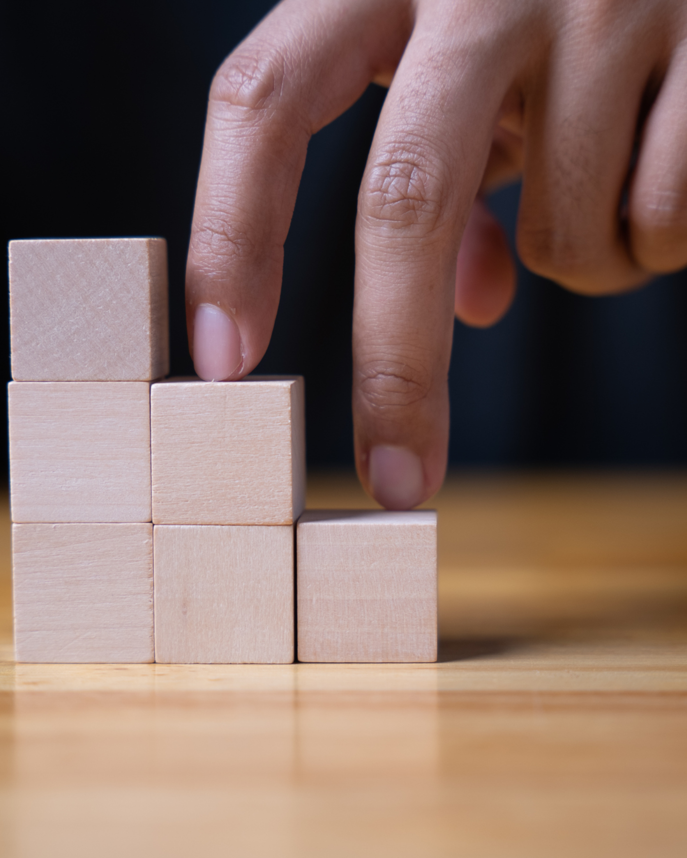Hand stacking wooden blocks on table.