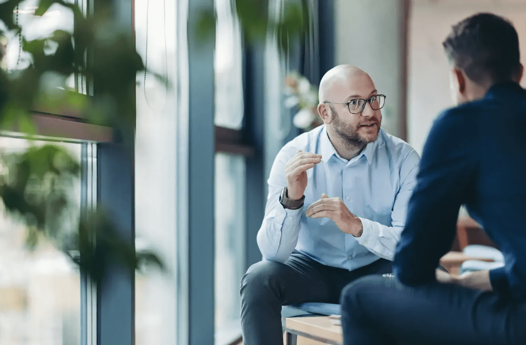 Two men having a discussion by window.