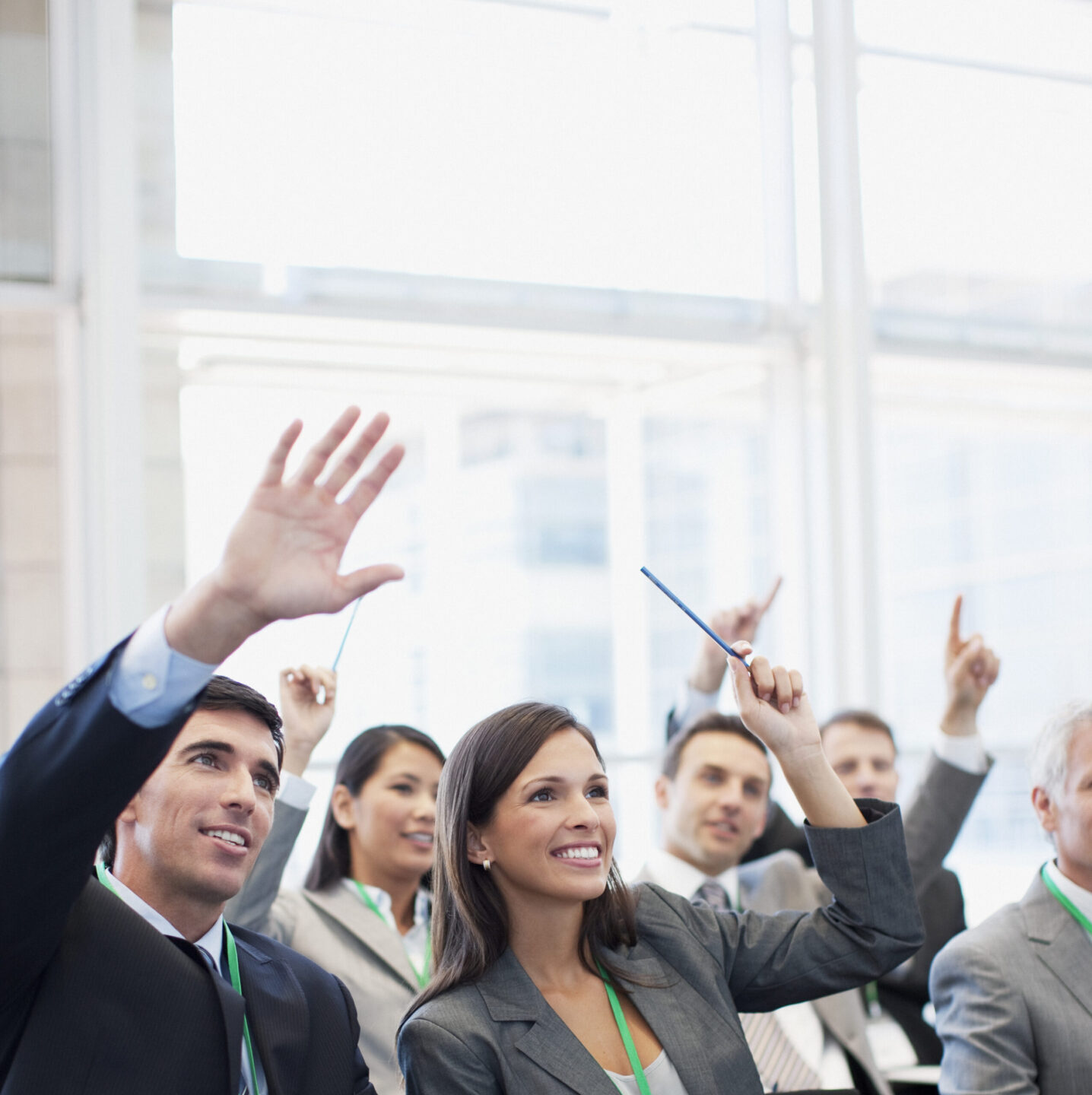 Business professionals raising hands in meeting.