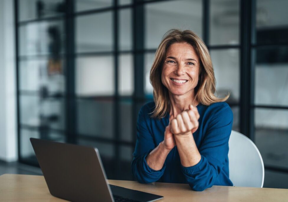 Smiling woman sitting at desk with laptop.