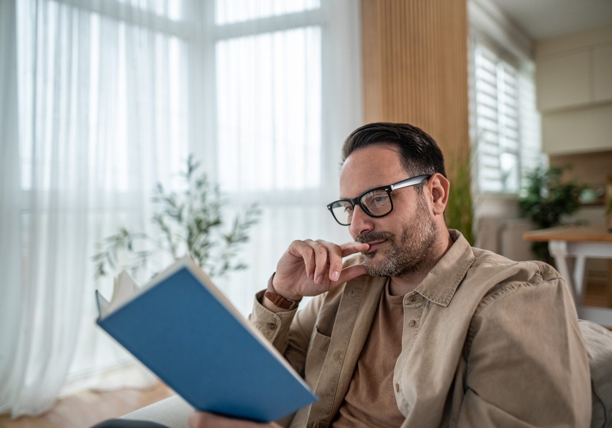 Man reading book in bright living room.